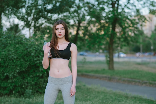 Mooi jong meisje met een mooie figuur atleet met een fles water in de hand. het meisje in een park jogt