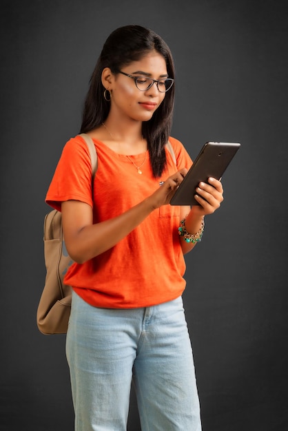 Mooi jong meisje met een rugzak met behulp van mobiele telefoon of smartphone op grijze achtergrond