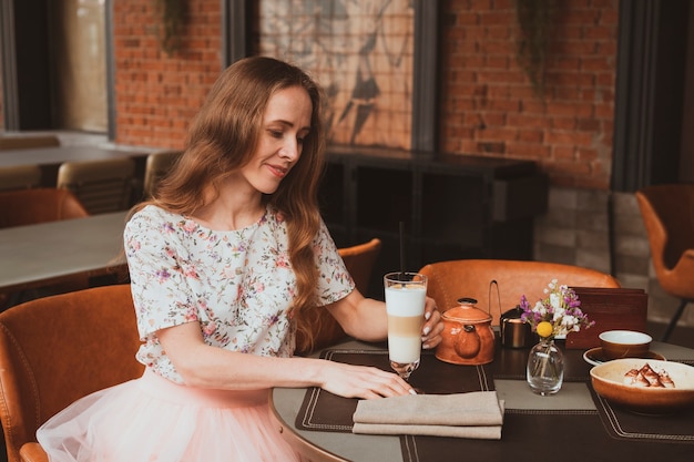 Mooi jong meisje met lang haar zit in een straatcafé en drinkt een kopje koffie