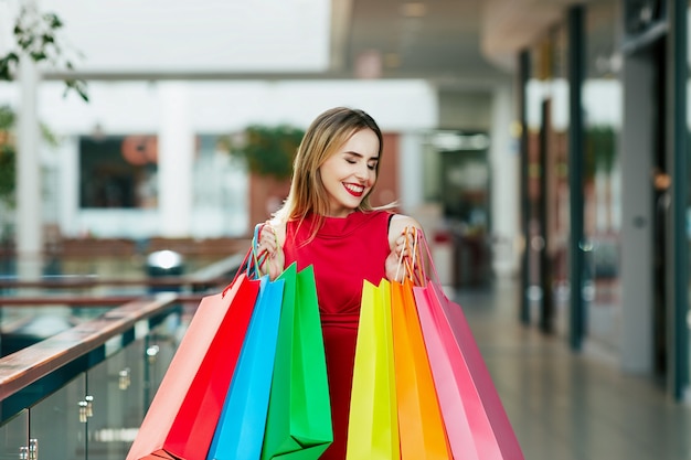 Mooi jong meisje met lichtbruin haar en rode lippen staan met kleurrijke boodschappentassen, shopping concept, portret, kopie ruimte, gelukkige emoties.