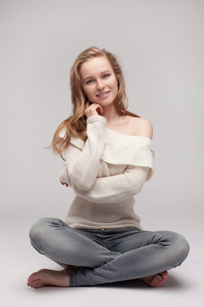 Mooi jong meisje poseren en zittend op een witte achtergrond. blond in een witte trui.