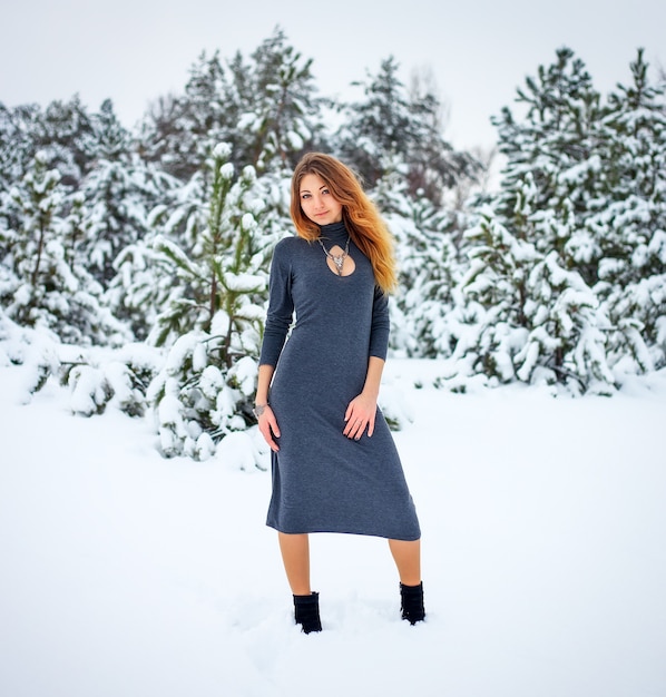 Foto mooi jong meisje poseren in de winter in koud besneeuwd bos met pijnbomen.