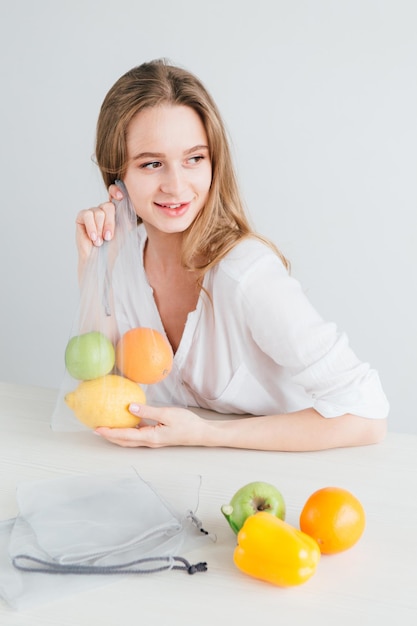 Mooi jong meisje verpakt de groenten en fruit in een herbruikbare stoffen zak. Het concept van nul afval. Tonen.