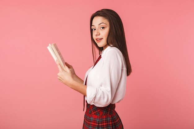 Mooi jong schoolmeisje die eenvormige status dragen die over roze muur wordt geïsoleerd