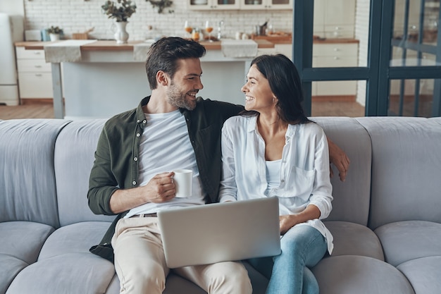 Mooi jong stel dat koffie drinkt en op de laptop kijkt terwijl ze thuis op de bank zitten