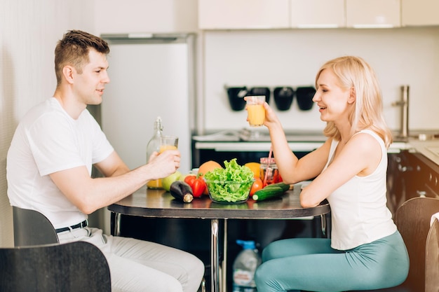 Mooi jong stel praat, kijkt naar elkaar en lacht terwijl ze ontbijten, verse jus d'orange drinken, samen een geweldige tijd hebben in de keuken thuis.