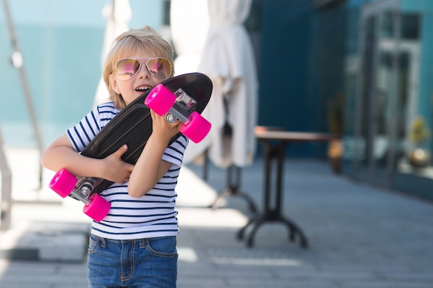 Foto mooi jongetje op een skate board. emotionele jongen buitenshuis. schattig kind schaatsen zonnebril dragen.