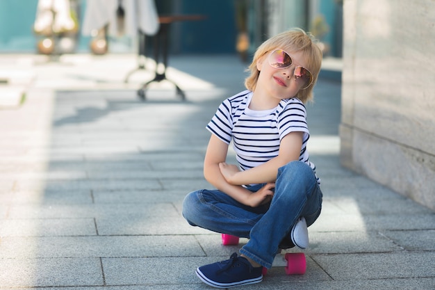 Mooi jongetje op een skate board. Emotionele jongen buitenshuis. Schattig kind schaatsen zonnebril dragen.