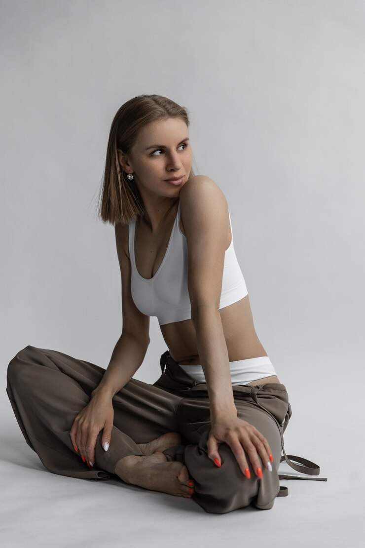 Mooi Kaukasisch meisje in witte lingerie en broek zit op een witte achtergrond in de studio en glimlacht