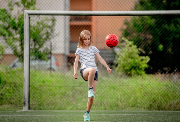 Mooi kind dat een voetbal schopt op het voetbalveld Leuk meisje dat een actief spel speelt