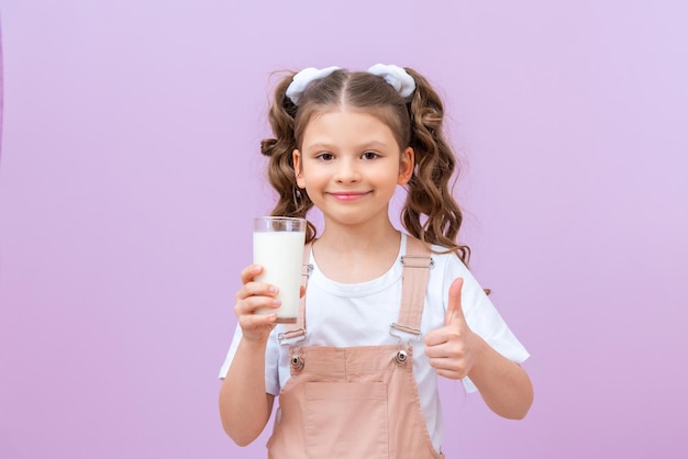 Mooi kind drinkt melk voor het ontbijt. Een klein meisje met krullend haar houdt een glas koemelk vast.