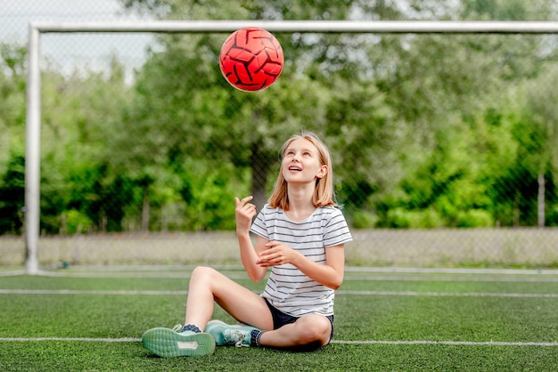 Mooi kind meisje zittend op gras en voetbal bal omhoog gooien Schattig vrouwelijk kind op socker veld spelen