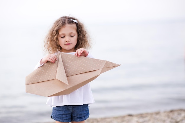 Mooi kindmeisje dat origamiwalvis over zeeachtergrond houdt