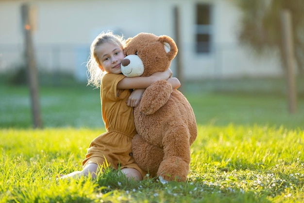 Mooi kindmeisje die teder haar teddybeervriend in openlucht op groen grasgazon omhelzen Concept vriendschapswaarden