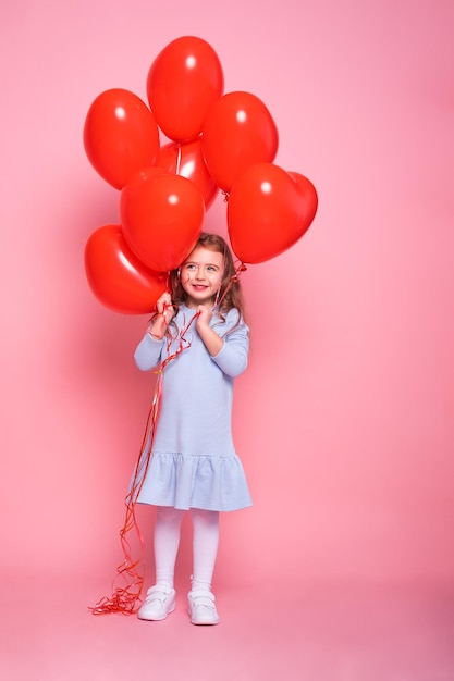Mooi kindmeisje met rood hart romantische ballons op roze achtergrondconcept valentijnskaartdag