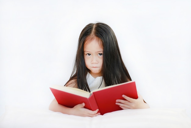 Mooi klein Aziatisch de lezings hardcover boek die van het kindmeisje met hoofdkussen op witte achtergrond liggen.