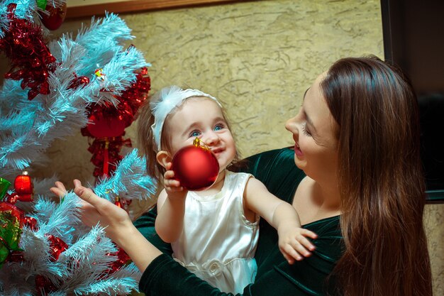 Mooi klein babymeisje met blauwe ogen versiert de kerstboom met haar moeder. kerststemming. nieuwjaar.