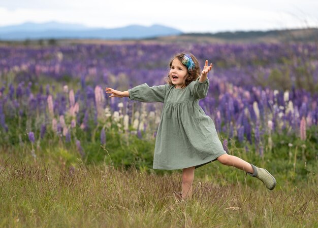 Foto mooi klein krullend meisje in groene jurk dansen op het gebied van lupine