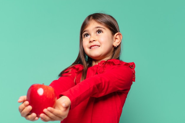 Mooi klein meisje dat uitdrukking denkt en een appel vasthoudt