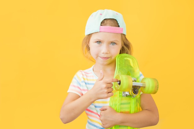 Mooi klein meisje dat zich op gele achtergrond met groene skate bevindt