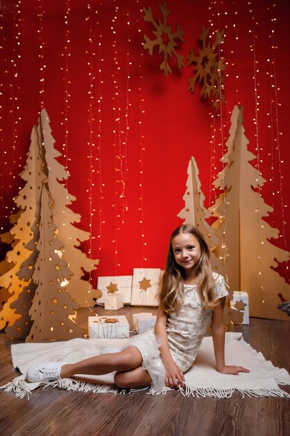 Mooi klein meisje droomt van kerstcadeaus. Rode kerstversiering, ongebruikelijk. De avond voor kerst, kerstavond