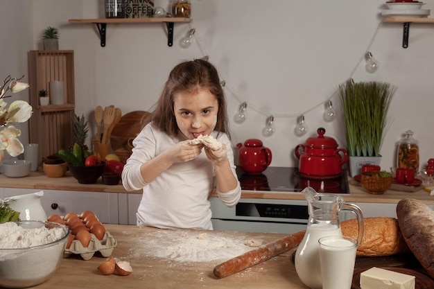 Mooi klein meisje gekleed in een witte blouse maakt een deeg voor het bakken van een brood in een keuken.