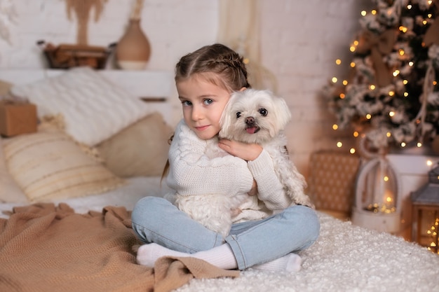 Mooi klein meisje heeft met staartjes op het hoofd een knuffel met haar favoriete maltese hond op bed