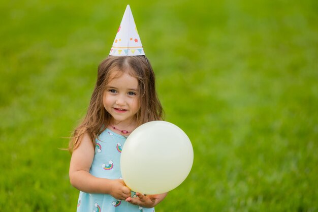 Mooi klein meisje in blauwe jurk en muts met ballonnen in park gelukkige verjaardag