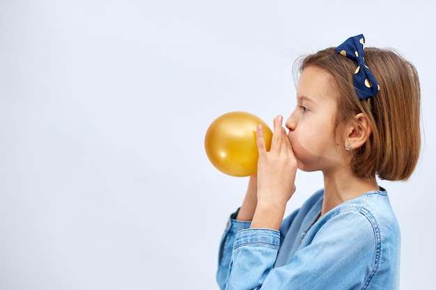 Mooi klein meisje in casual denim jurk waait gele ballon opblazen