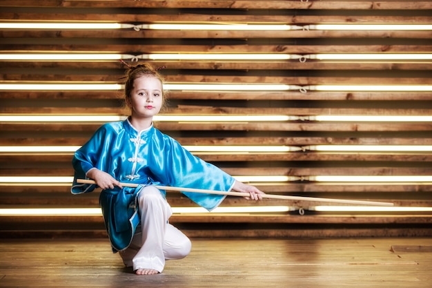 Mooi klein meisje in de kamer in sportkleding voor vechtsporten is Wushu of kungfu