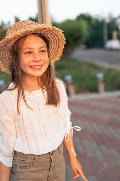 Mooi klein meisje in de stad bij zonsondergang Het meisje in een witte blouse en met een strohoed glimlacht en verheugt zich in het leven