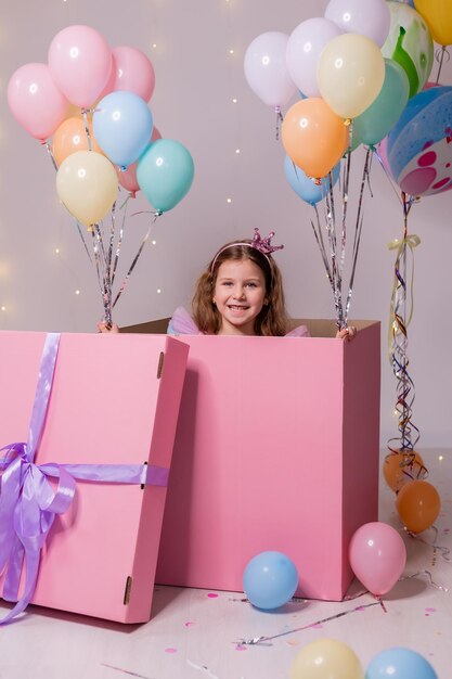 Foto mooi klein meisje in een kleurrijke jurk met ballonnen speelt in een enorm roze verrassingsdoosje kind