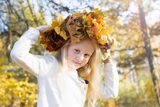 Mooi klein meisje in een krans met herfstbladeren Kind op een wandeling in het park
