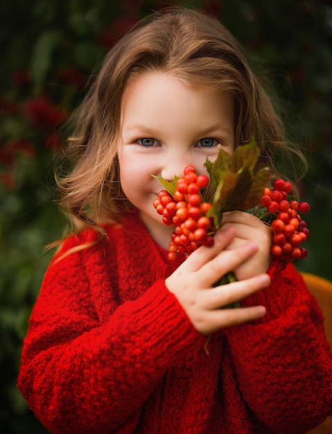 mooi klein meisje in een rood gebreid jasje met mountain ash herfstpark