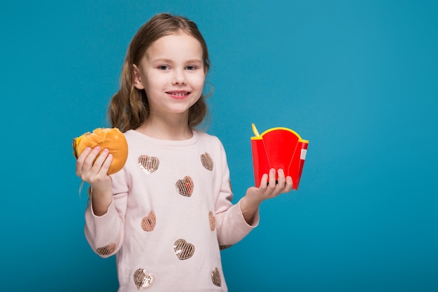 Mooi, klein meisje in trui met donkerbruin haar houdt een hamburger