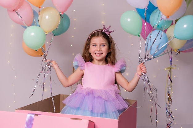 Mooi klein meisje met ballonnen springt uit een enorme roze doos kind viert zijn verjaardag