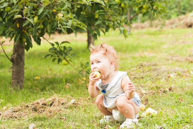 Mooi klein meisje met een appel in de hand, staande onder de appelboom