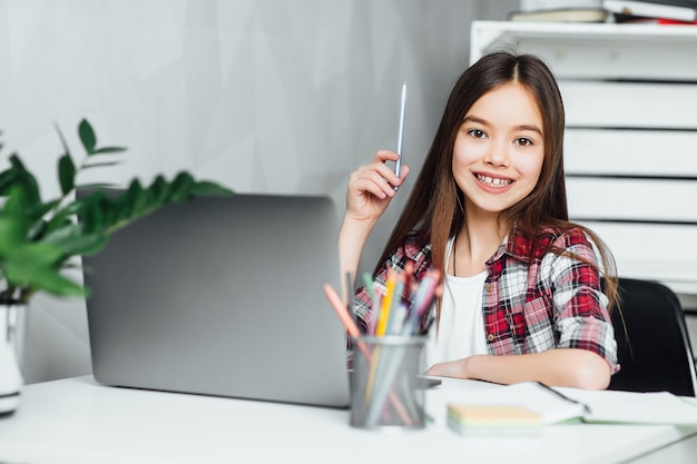 Mooi klein meisje met potlood bij de hand met behulp van notebook tijdens het voorbereiden van huiswerk