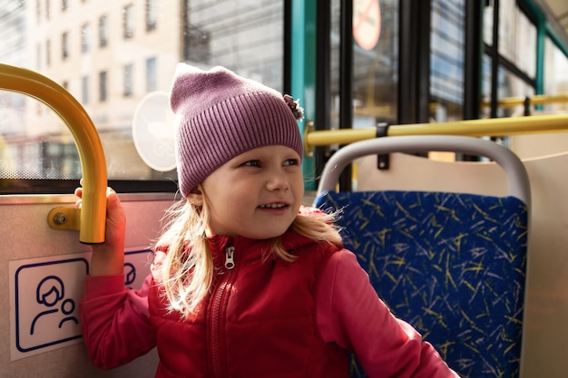 Mooi klein meisje rijdt bus van openbaar modern vervoer kijkt uit raam Kind in grootstedelijk vervoer