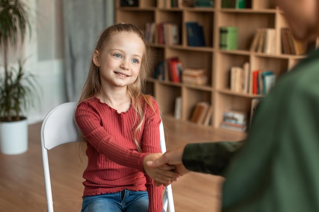 Mooi kleutermeisje dat psychotherapeute vrouw en kind bezoekt die handen schudden voor de sessie op kantoor