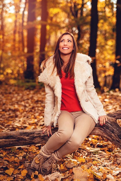 Mooi lachend meisje genieten in het bos in de herfst. Ze zit in de boom en denkt na.