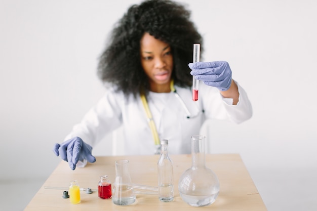 Mooi meisje arts in een witte jas met een stethoscoop. zitten aan een tafel met reagens kolven op witte achtergrond. Vrouwenonderzoeker die een bloedonderzoek in een laboratorium doen