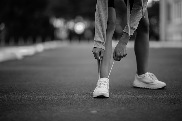 mooi meisje atleet zit veters vast te binden op witte sneakers zwart-wit foto