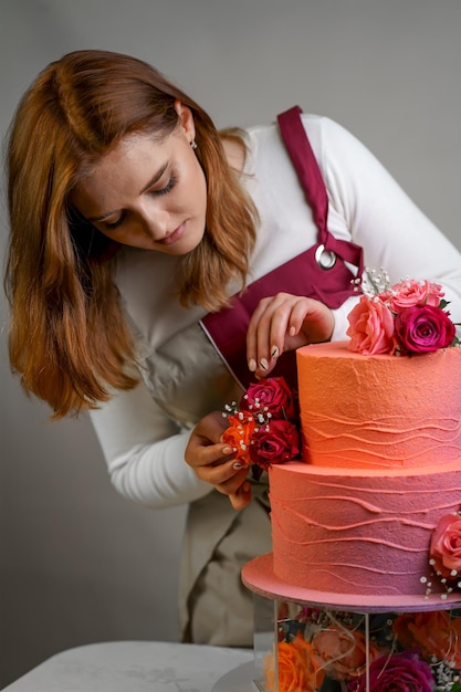Mooi meisje banketbakker in een werkschort versiert een verjaardagstaart met verse bloemen