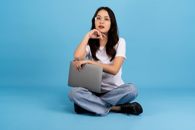 Mooi meisje blij met een notebookcomputer zittend op een blauw