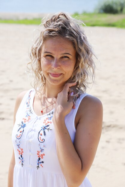 Mooi meisje, blond met haar dat zich ontwikkelt uit de wind tegen de zanderige kust