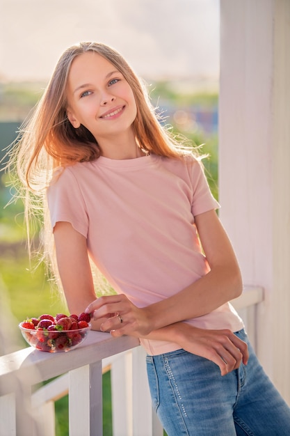 Mooi meisje, blond, tiener met lang haar op een zomeravond eet aardbeien op de veranda