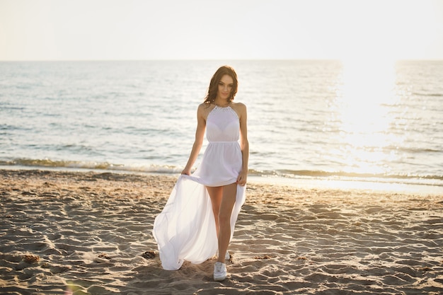 Mooi meisje bruid in een witte jurk en sneakers, bij zonsondergang wandelingen langs het strand.