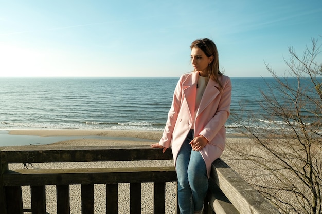 Mooi meisje dat aan de kust loopt met koffie Meisje loopt aan zee met koffie Mooi blond Vrolijk meisje met mooi haar in de zon