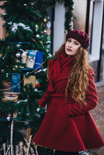 Mooi meisje dat een rode laag en een baret op Kerstmisstraat draagt